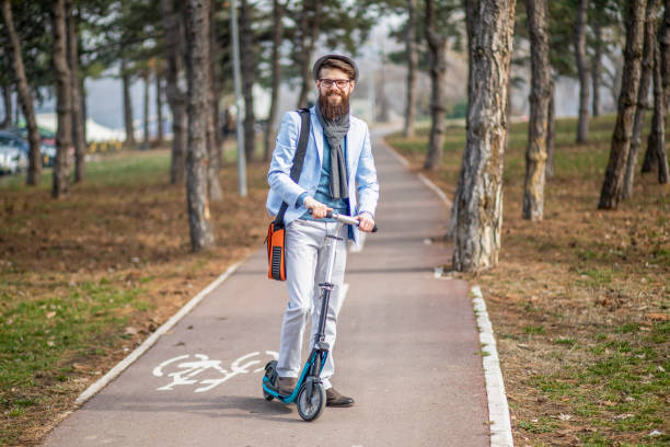 istock Young businessman with a beard on a kick scooter holds a white phone 1132651667