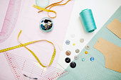 Yellow measuring tape, blue thread, colorful buttons, light blue cloth and cardboard pattern are lying in white table