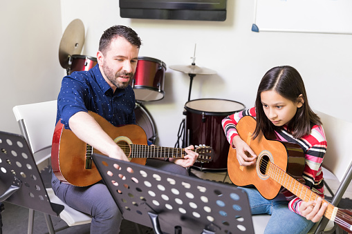 Music teacher giving instruction in instrumental music to preteen girl at guitar class
