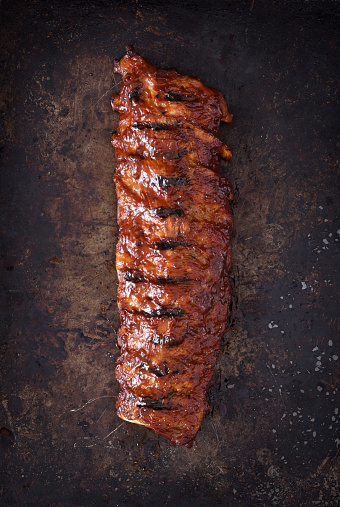 Full rack of grilled barbecue ribs with barbecue sauce on a dark background