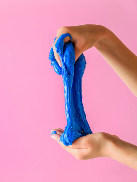 The child stretches slime blue on a pink background. The child stretches slime blue on a pink background. Toy antistress. Toy for the development of hand motor skills. slimy stock pictures, royalty-free photos & images