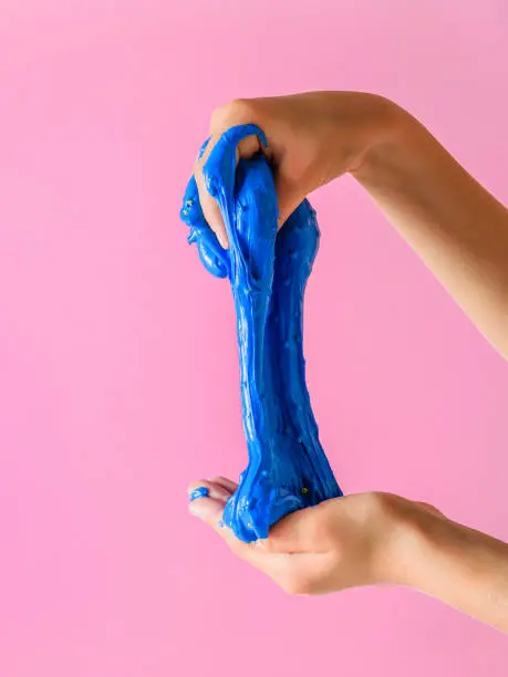Photo of The child stretches slime blue on a pink background.