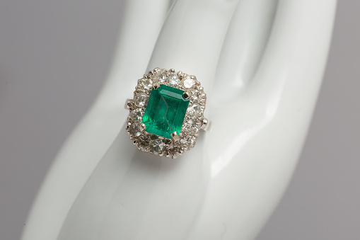 A shiny green emerald gemstone surrounded by diamonds on a silver ring retail display close up