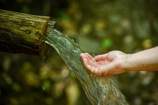 Image of drinking clean cold spring flowing water in nature during spring/summer time. Female hand is collecting the water for drinking. Close up shot with no recognizable face
