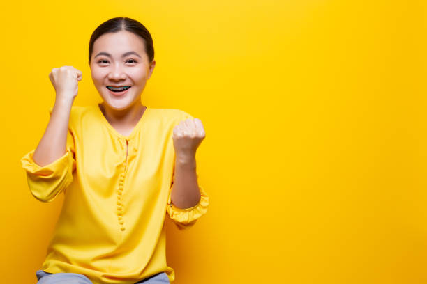 istock Happy woman make winning gesture isolated over yellow background 1132675376