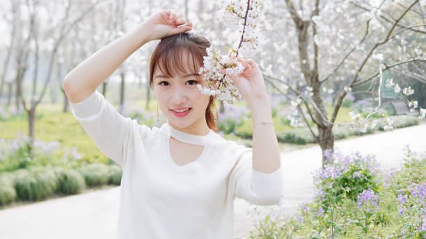 portrait extérieur de la belle jeune fille chinoise souriant parmi le brunch de cerisier de fleur dans le jardin de printemps, la beauté, l'été, l'émotion, l'expression et le concept de mode de vie de personnes. - cherry blossom flower head spring flower photos et images de collection