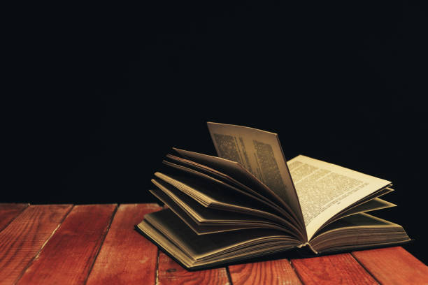 istock One open old book on a red wooden table. Beautiful dark background. 1132686993