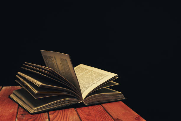 istock One open old book on a red wooden table. Beautiful dark background. 1132687073