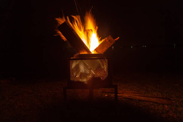 Backyard campfire in brazier against night sky with lights in the background - isolated, family fun in autumn or spring, holiday, sleepout and camping activity under supervision. Landscape format inspiration for relaxation