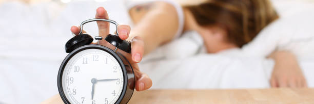 istock Sleepy young woman trying kill alarm clock 1132700822