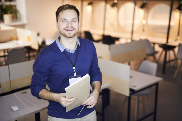 istock Optimistic confident handsome young man with badge on neck holding papers and smiling at camera 1132704446