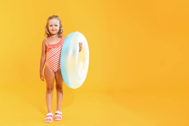 портрет счастливой маленькой девочки в купальнике с плавательным кольцом на цветном желтом фоне. концепция отпуска - inflatable floating on water life belt equipment стоковые фото и изображения