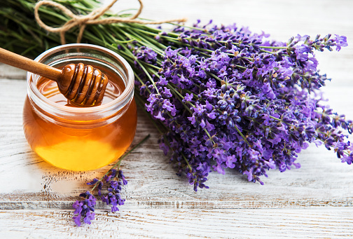 Jar with honey and fresh lavender flowers on a white wooden table