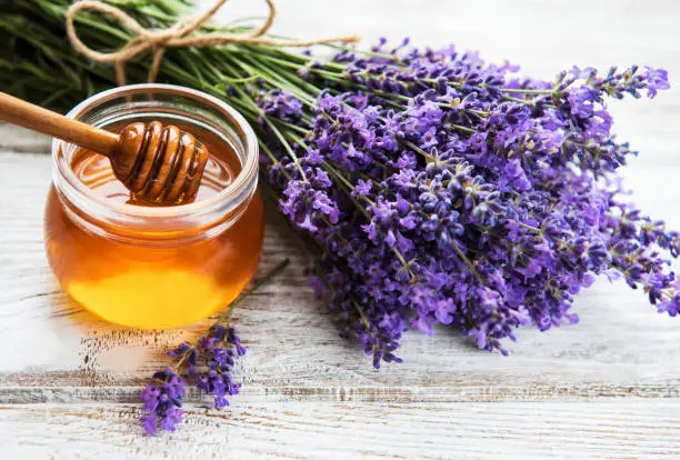 Jar with honey and fresh lavender flowers on a white wooden table