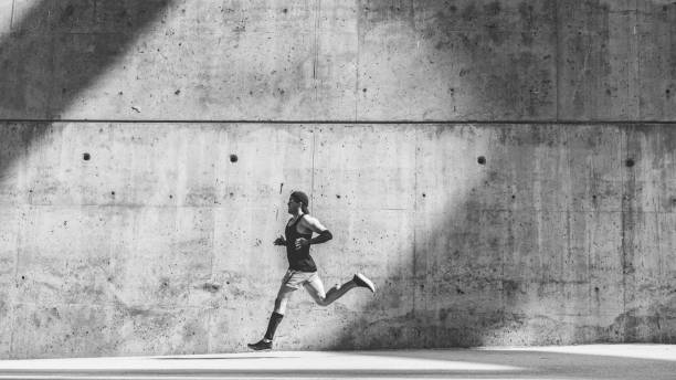 istock Muscular man athlete sprinter running fast,exercising outdoors,jogging outside against gray concret background with copy space area for text message or ad content.Wide,full length.Black white. 1132714681