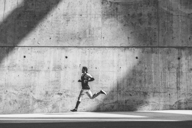istock Muscular man athlete sprinter running fast,exercising outdoors,jogging outside against gray concret background with copy space area for text message or ad content.Side view,full length.Black white. 1132714684