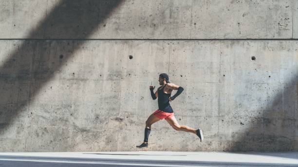 istock Muscular Male athlete sprinter running fast,exercising outdoors,jogging outside against gray concret background with copy space area for text message or advertising content.Side view,full length.Wide. 1132714694