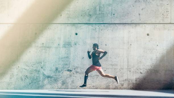 istock Muscular Male athlete sprinter running fast,exercising outdoors,jogging outside against gray concret background with copy space area for text message or ad content.Side view,full length.Wide. 1132714703