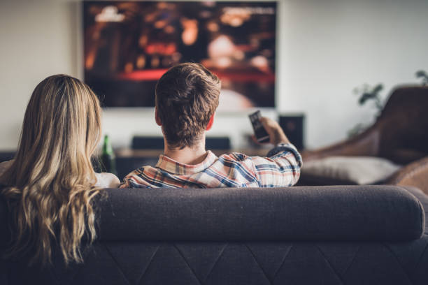 vista posteriore di una coppia che guarda la tv mentre si rilassa sul divano a casa. - guardare la tv foto e immagini stock