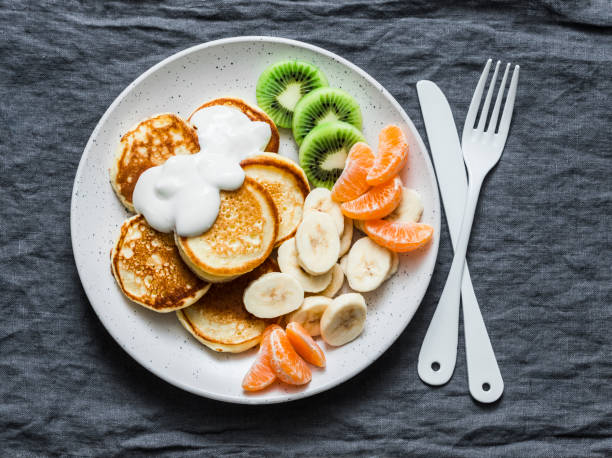 istock Delicious breakfast or snack - pancakes with fruit and sour cream on a grey background, top view. Baby food 1132718334