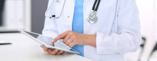 istock Unknown doctor woman at work. Female physician using digital tablet  while standing near reception desk at clinic or emergency hospital. Medicine and healthcare concept 1132719238