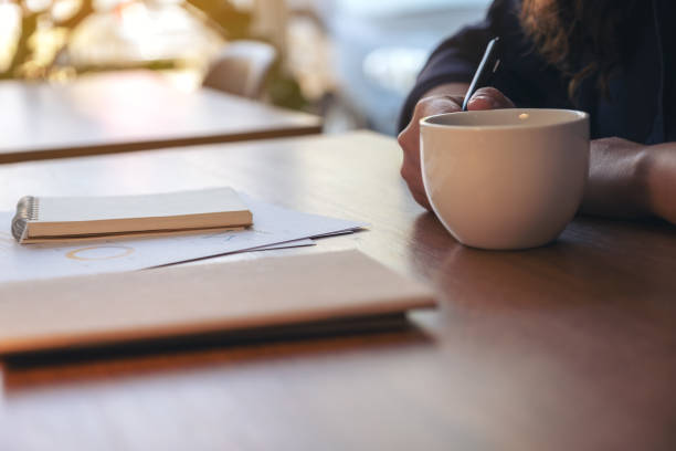istock Closeup image of a woman's hand holding a cup of hot coffee while working on business document on wooden table 1132720007