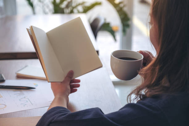 istock Closeup image of a woman holding and opening a blank notebook while drinking coffee 1132720035