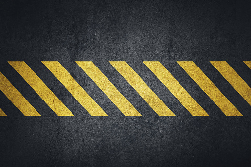 Old black grungy metal plate surface with yellow warning stripes in center. Building, construction. Banner, place for text.