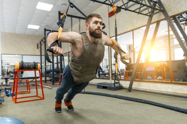 istock Muscular bearded man dressed in military weighted armored vest doing exercises using straps systems in the gym. Sport, training, bodybuilding and healthy lifestyle concept. 1132728856