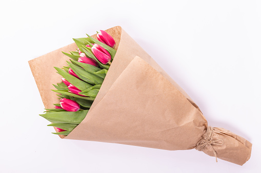 Bouquet of spring tulips with pink flowers wrapped in paper for present on white background