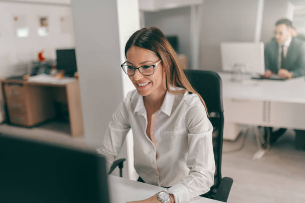 istock Young Caucasian secretary in shirt and with eyeglasses using computer for work. In background employee working. I'm in corporate business. What is your superpower? 1132731868