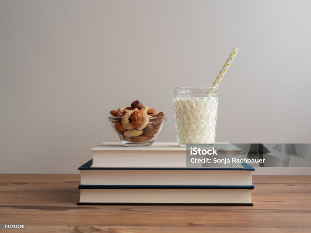 Bust stack with a glass of milk and a bowl of nuts food, book, dairy product, student food, learning, school, wooden table, white background, text space, reading Trail Mix Stock Photo