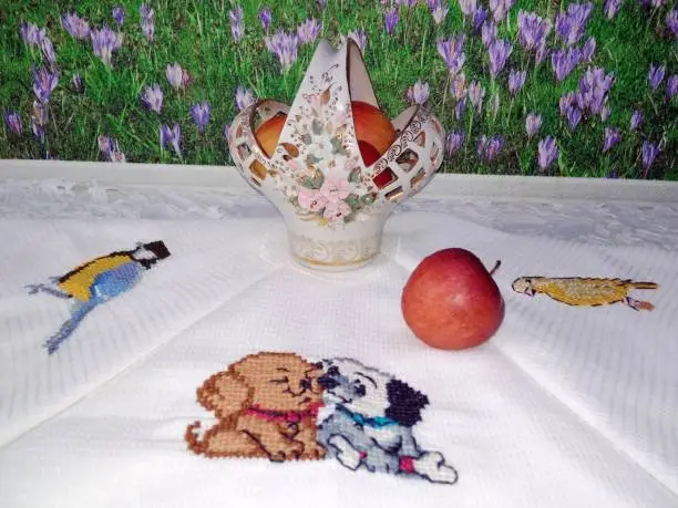 Beautiful kitchen service on the embroidered towels. A vase with apples against the background of flower wall-paper.