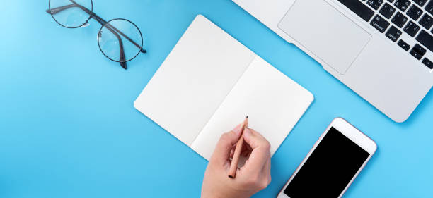 istock A student write on open white book or accounting isolated on a minimal clean blue workplace at home with smartphone and accessories, copy space, flat lay, top view, mock up 1132735993