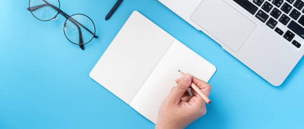 istock A student write on open white book or accounting isolated on a minimal clean blue workplace at home with smartphone and accessories, copy space, flat lay, top view, mock up 1132736072