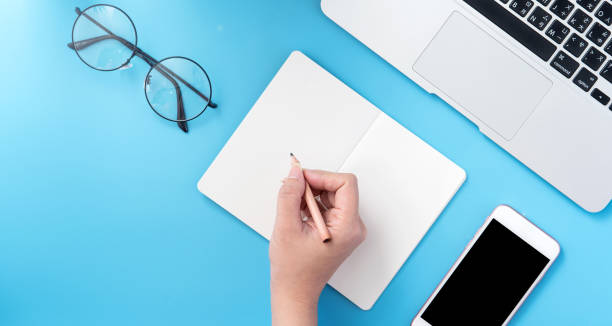 istock A student write on open white book or accounting isolated on a minimal clean blue workplace at home with smartphone and accessories, copy space, flat lay, top view, mock up 1132736372