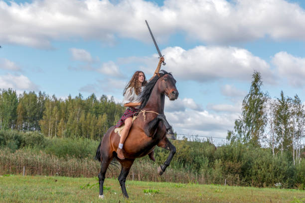 chica en un kilt escocés sosteniendo una espada en su mano a caballo, que cuesta en obstaculizar las piernas - hinder fotografías e imágenes de stock