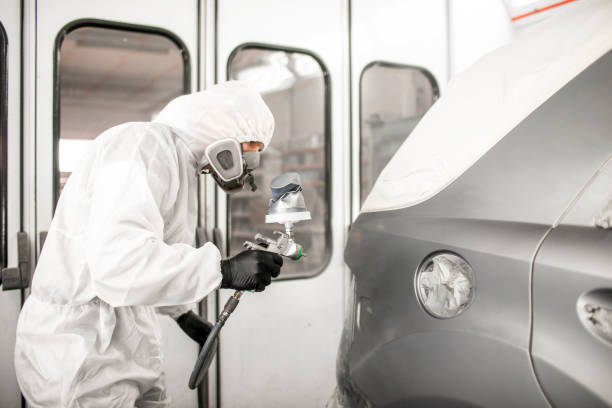 Car painter in white overalls spraying a car body with paint Professional car painter blasting a car part with a base coat paint in a workshop. door panel stock pictures, royalty-free photos & images