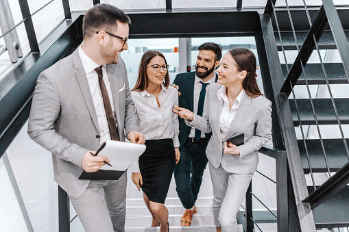 Four happy colleagues in formal wear climbing the stairs and talking about business. Corporate business concept. Let the teamwork makes dream come true.