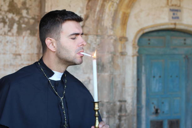 priest lighting a cigarette with a candle - bad habit imagens e fotografias de stock