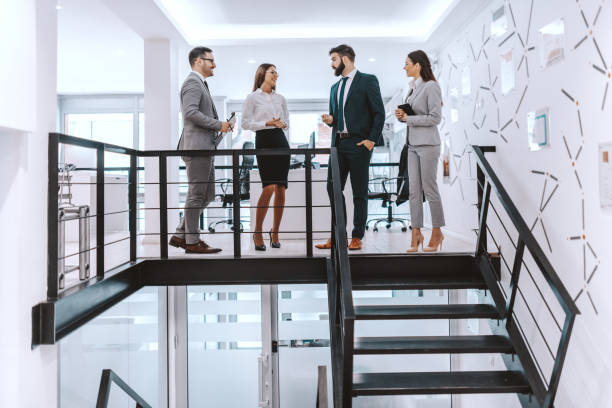 istock Four smiling colleagues in formal wear standing at modern work place and chatting. A successful team beats with one heart. 1132747114