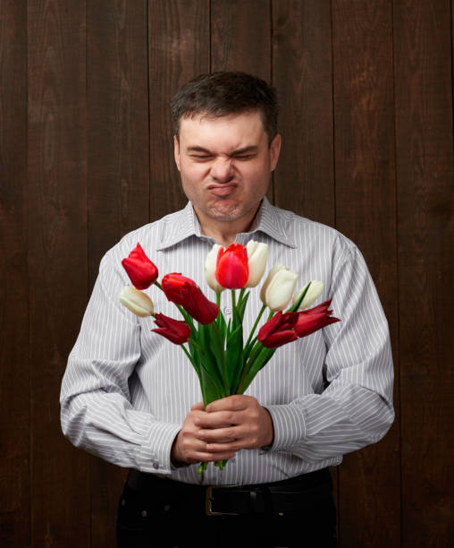 man holds red flowers bouquet with awful smell - facial expression unpleasant smell shirt caucasian imagens e fotografias de stock