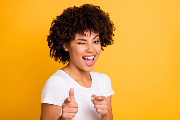 cerrar foto bastante increíble ella su piel oscura señora brazos dedos punto en usted recogiendo divertido funky guiándose un ojo risa risas usando casual camiseta blanca aislado amarillo brillante fondo vivo - parpadear fotografías e imágenes de stock