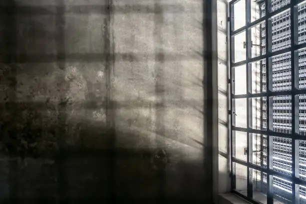 Photo of The very sober interior of a prison cell: barred windows with little light coming in and bare concrete walls