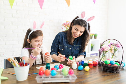 Smiling woman and daughter decorating eggs to be used as gifts on the occasion of Easter