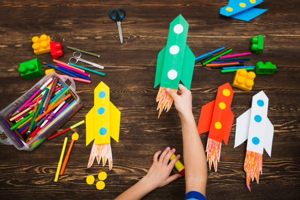 아이는 나무 테이블의 배경에 대해 종이로 만든 로켓을 보유 하 고 있습니다. 가정에서 창의력에 유치원 아이. 행복 한 아이는 종이에서 로켓을 만든다. 아 이들의 창의력. - art and craft 뉴스 사진 이미지