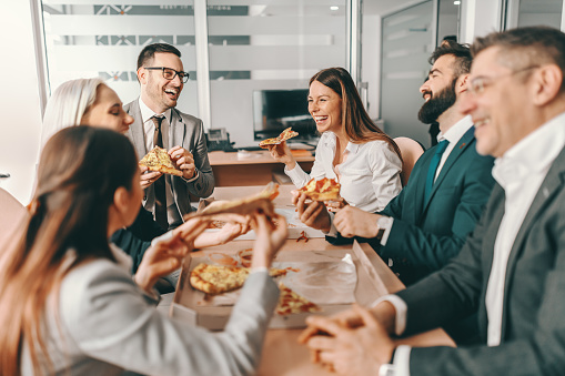 Pequeño grupo de colegas felices en el uso formal charlando y comiendo pizza juntos para el almuerzo. Solos podemos hacer tan poco, juntos podemos hacer tanto. photo