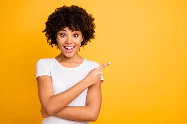 Photo of Portrait of her she nice cute lovely charming attractive cheerful cheery glad optimistic wavy-haired girl pointing aside copy space isolated on bright vivid shine yellow background