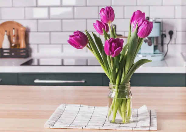 Photo of Purple tulips in a glass jar standing on the modern kitchen