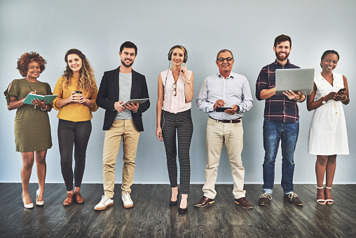 Shot of a group of business people using their smart devices while standing against a wall